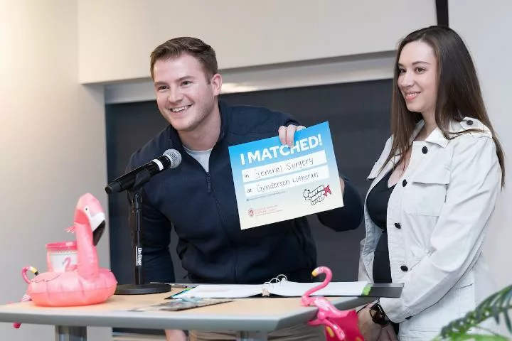 Spencer Treu holds up an "I Matched!" sign at the podium