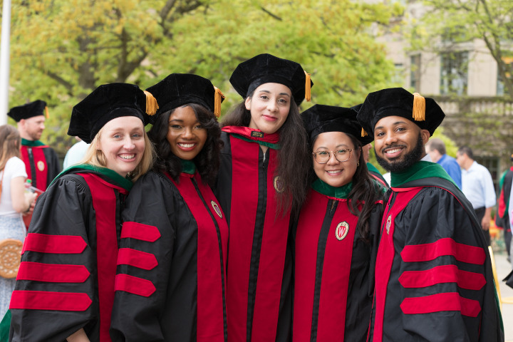 A group of graduates in their robes smiling and huddling together for a picture