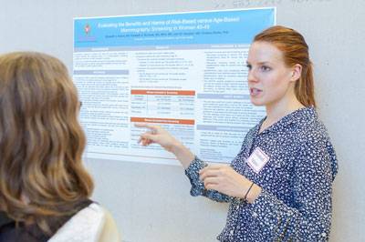 A student discusses their research next to their poster