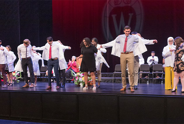 Six incoming medical students being helped into white coats by faculty
