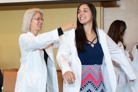 A proud health professional cloaks a student in a white coat