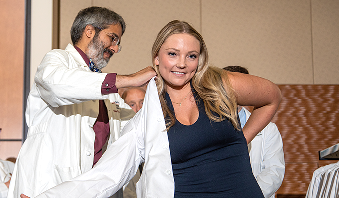 A PA student is helped into a white coat at the 2023 White Coat Ceremony
