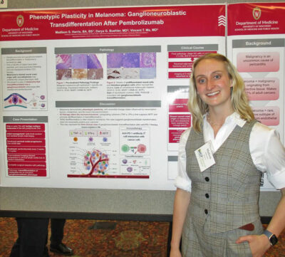 Madison Harris smiles in front of her research poster titled Phenotypic Plasticity in Melanoma