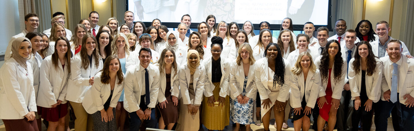 A large group of smiling students in their white coats