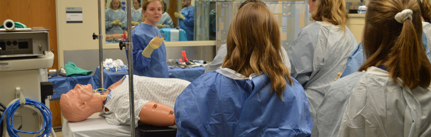 Students dressed in PPE practice their skills with a manikin