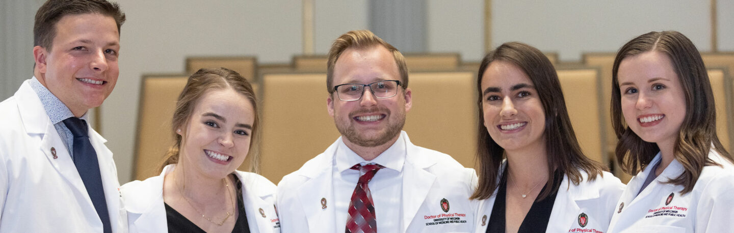 Students smile for a photo in their white coats