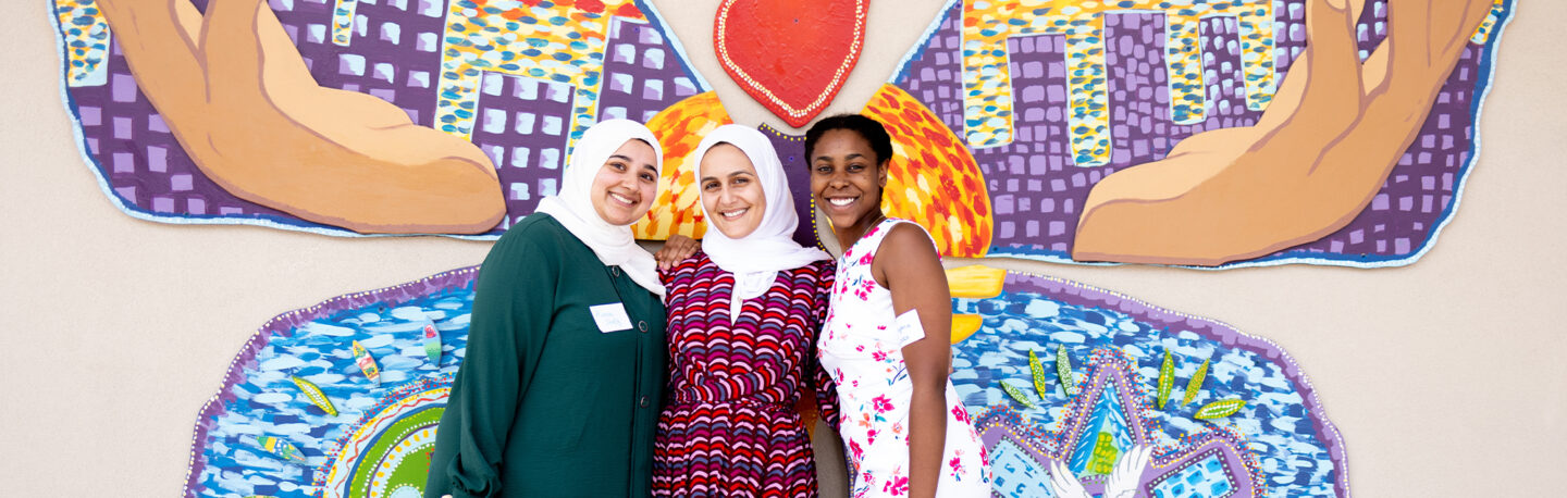 Three women smiling for a photo in front of a mural