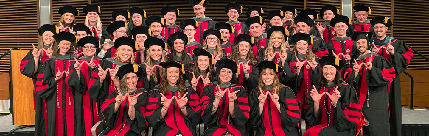 A large group of graduates, now DPT alumni, smiling together in their caps and gowns