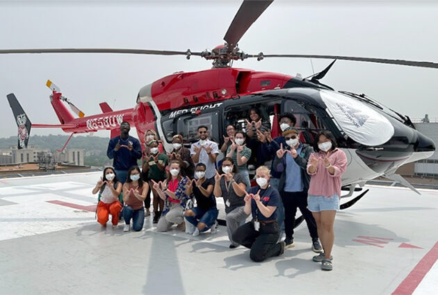 A group of Badger students posing for a photo in front of an emergency medicine helicopter