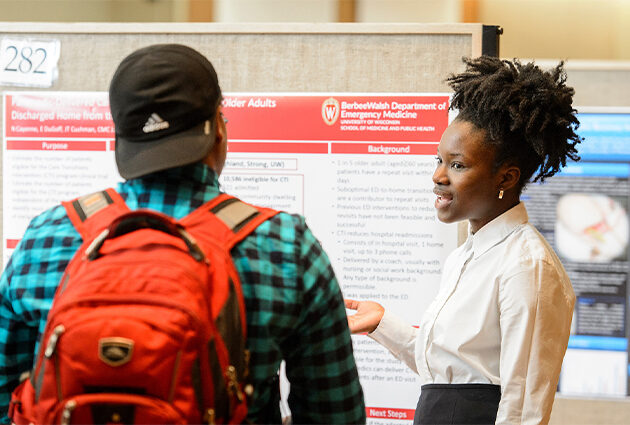 A student presenting their research poster to another person