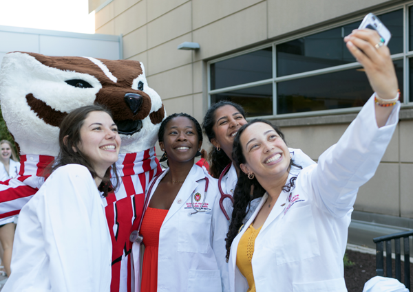 Students take a selfie with Bucky Badger in their white coats and new stethoscopes