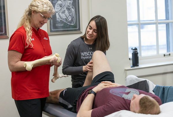 A DPT instructor demonstrates a technique to a student with a skeleton leg