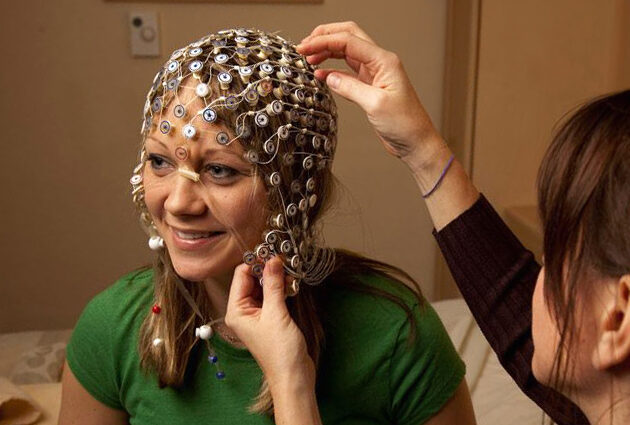 A person positions a cap made of electrode discs on a woman's head for a sleep study