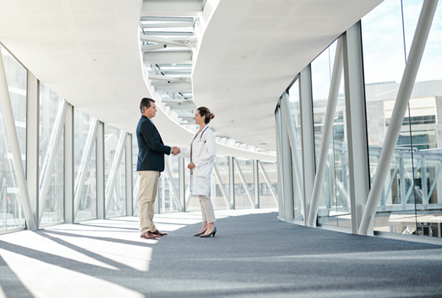 A doctor shaking hands with a person in a suit in an enclosed elevated walkway