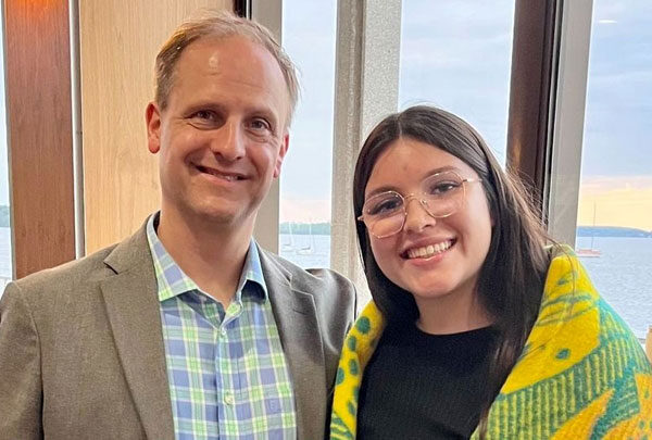 Tashelle Peigan with a blanket around them smiles with Jeff Hartman at the Native American Center for Health Professions graduation blanket ceremony