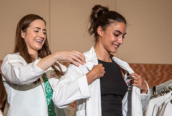 A student smiles while putting on their new white coat