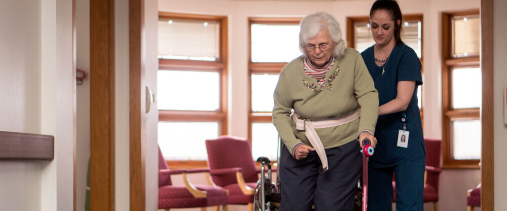 A health care worker using a gait belt to help an elderly woman