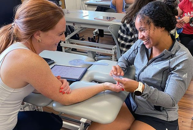 A DPT student smiles and holds out a skeleton arm