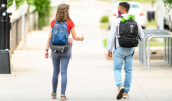 Two students walk down the sidewalk together while social distancing