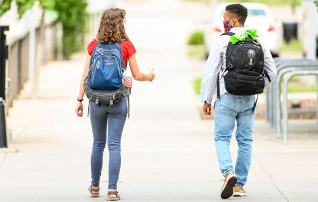 Two students walk down the sidewalk together while social distancing