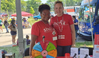Two workers smile together at a booth for a community event