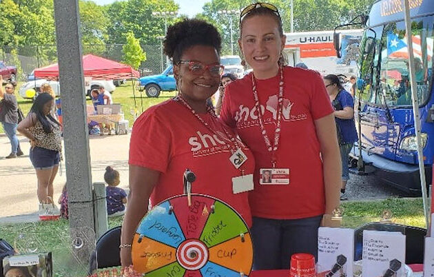 Two workers smile together at a booth for a community event