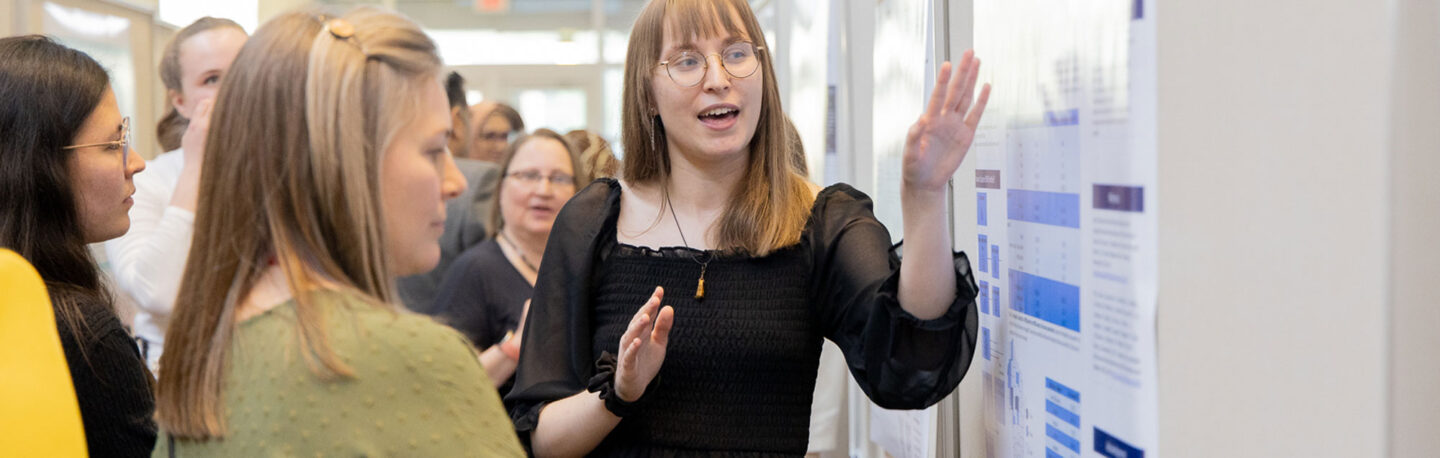 Student gesturing and speaking with others about a poster