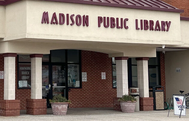 Exterior of a Madison Public Library with a "Vote Here" sign on the sidewalk
