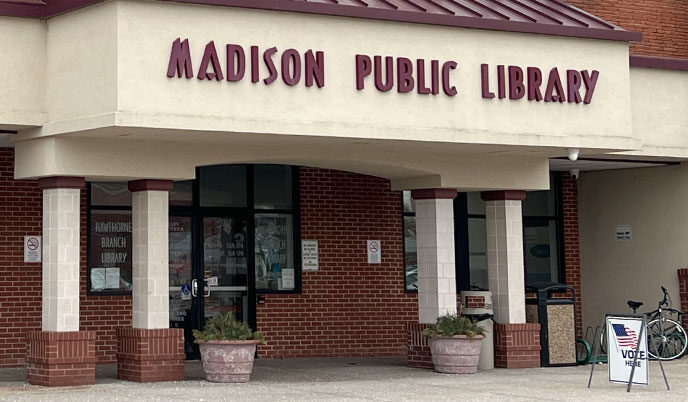 Exterior of a Madison Public Library with a "Vote Here" sign on the sidewalk