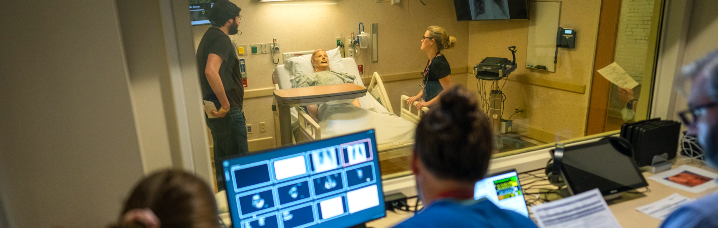 Three people observe while two others work with a training mannequin during a global health simulation