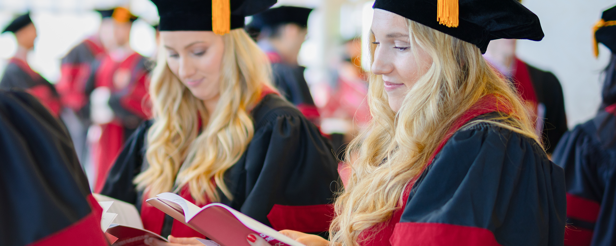 Two graduates, in caps and gowns, look through their programs before the celebration