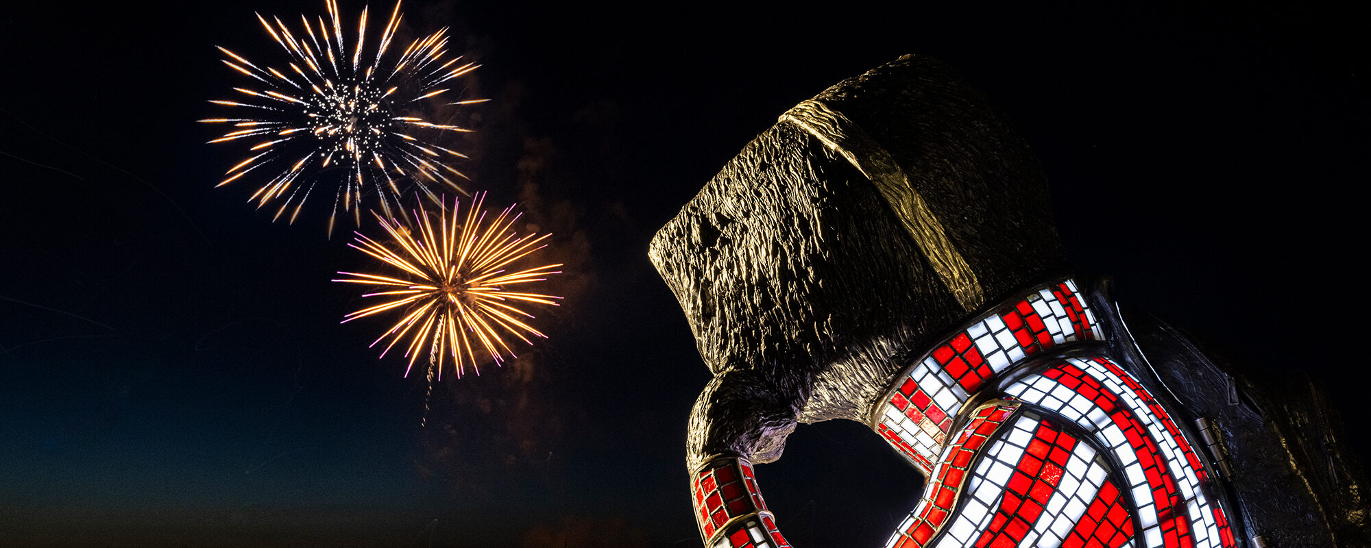 A statue of Bucky Badger looking out into the night, where fireworks are going off