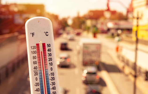 A thermometer showing 102 degrees Fahrenheit with urban traffic and buildings in the background