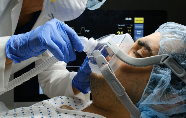 The gloved hand of a hospital employee adjusts a patient's ventilation mask