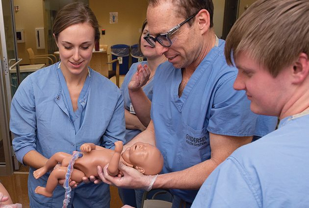 Rural medicine MD students and an instructor carefully hold a manikin of a newborn