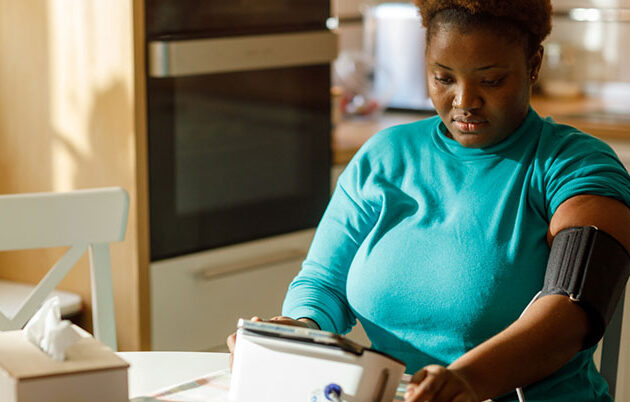 A woman using a blood pressure monitor at home.