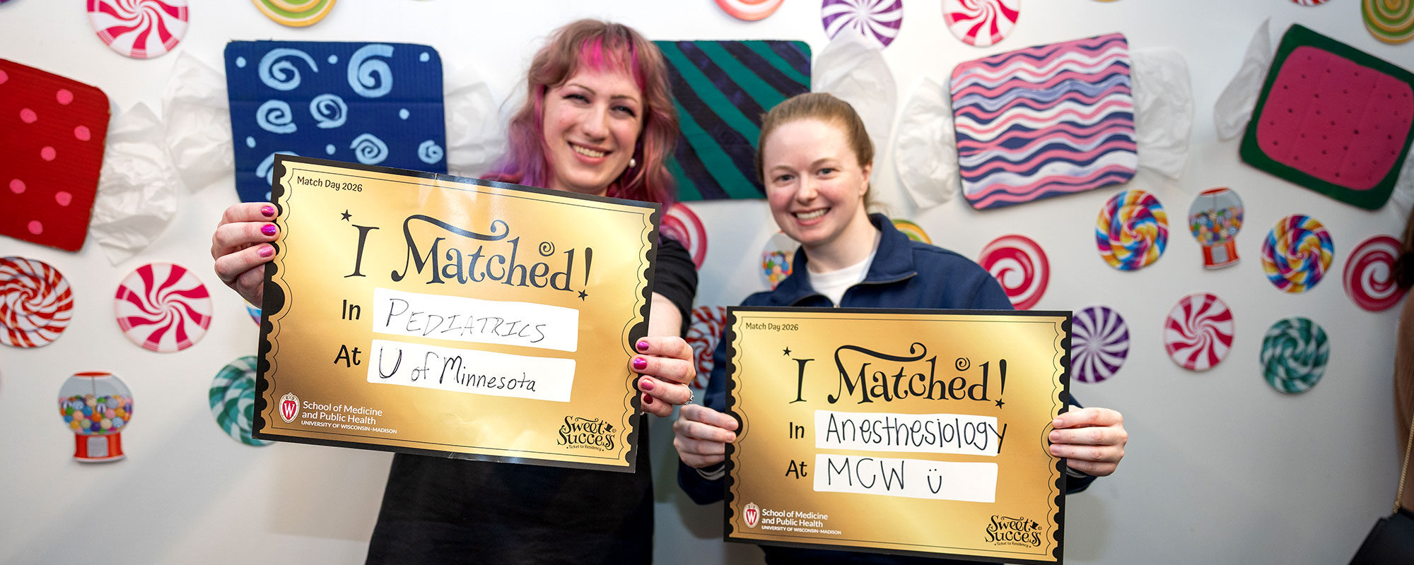 Two medical students smiling big and holding signs indicating where they matched: Pediatrics at University of Minnesota and Anesthesiology at MCW.