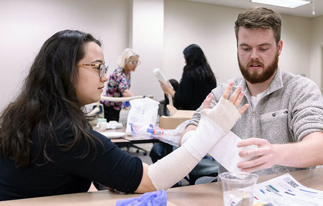 A student wraps another students arm in a bandage at the annual Family Medicine Procedures Fair.