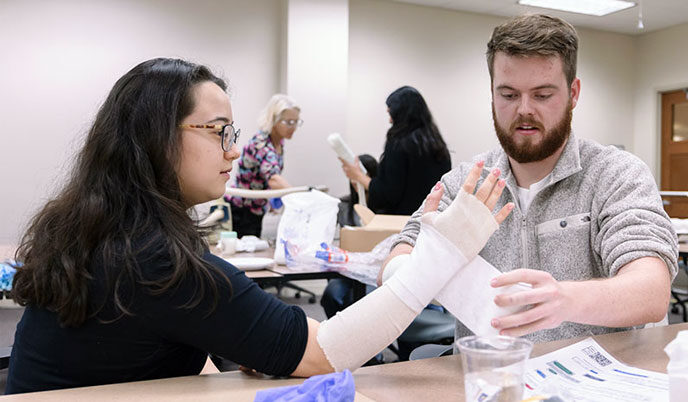 A student wraps another students arm in a bandage at the annual Family Medicine Procedures Fair.