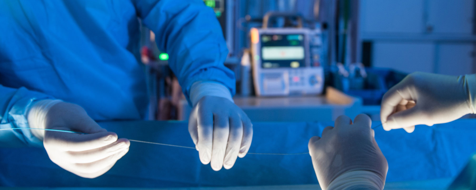 Two people with gloved hands holding a stent in an operating room.