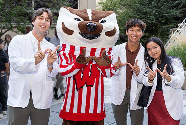 Students in white coats smile with Bucky Badger