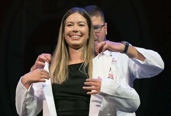 A student happily dons their white coat for the first time