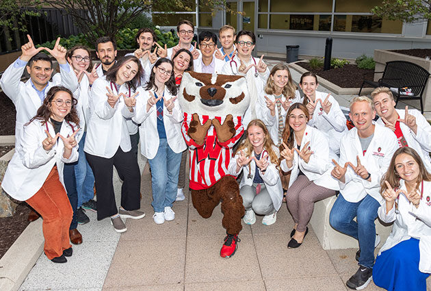 A large group of students in white coats posing with Bucky Badger