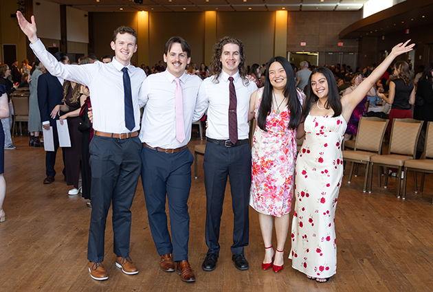 Five people wearing dress attire smile at an event.