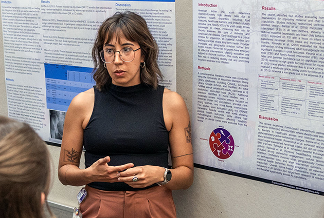 A woman presents to an onlooker while standing in front of a poster