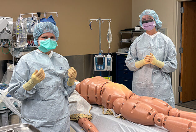 Two physician assistant students in PPE practice surgical skills with a manikin