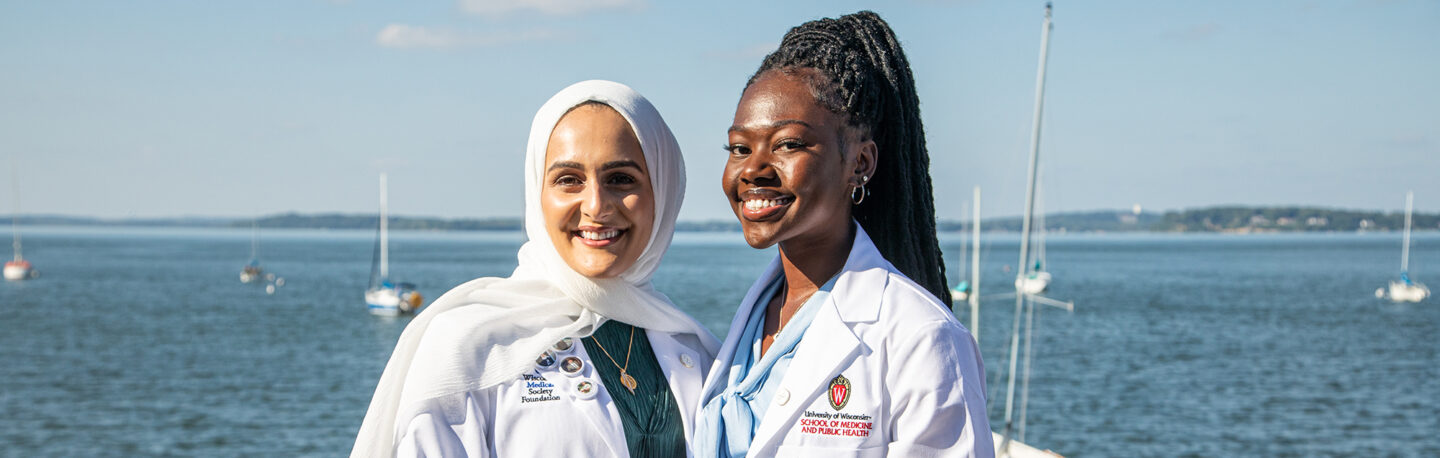 Two medical students in their white coats smiling together on the Madison lakefront
