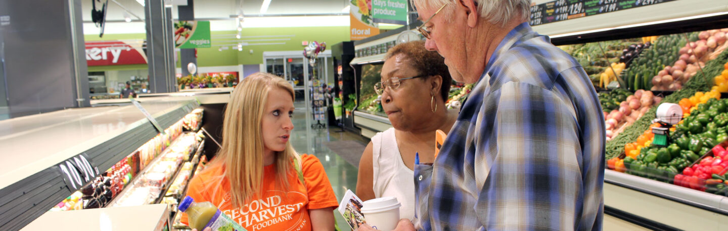 A student in a conversation with two attentive listeners, in a produce aisle