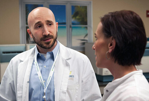 Two people in professional wear and white coats having a discussion